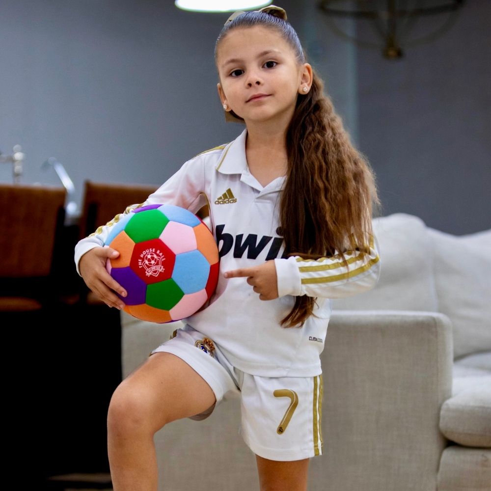 Young girl in sports uniform holding a colorful ball in a living room.